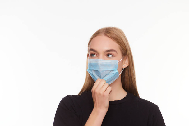 blond young woman wearing medical mask adjusting it with her hands close up isolated white background - Photo, Image