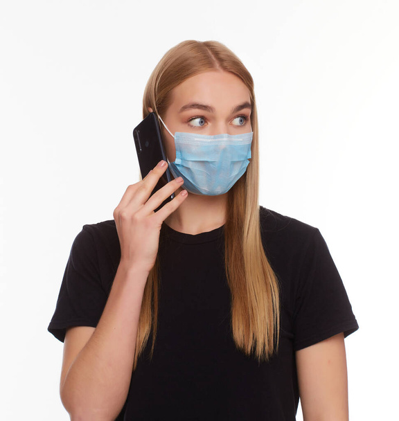 European Girl in a Maske benutzt ein Telefon. Konzeptfoto zum Thema Epidemie. Isoliert auf weißem Hintergrund. - Foto, Bild