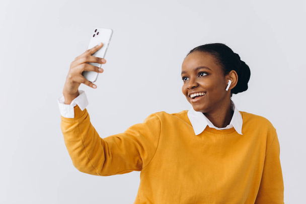 Jeune femme noire mignonne avec dreadlocks élégant prendre selfie sur smartphone pour les médias sociaux ou amis, femme afro-américaine positive s'amuser à la maison, en utilisant un téléphone mobile, espace de copie - Photo, image