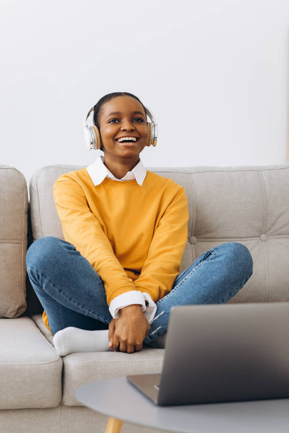 Jovem afro-americana falando em vídeo chamada na sala de estar em casa, conceito de educação à distância de casa. - Foto, Imagem