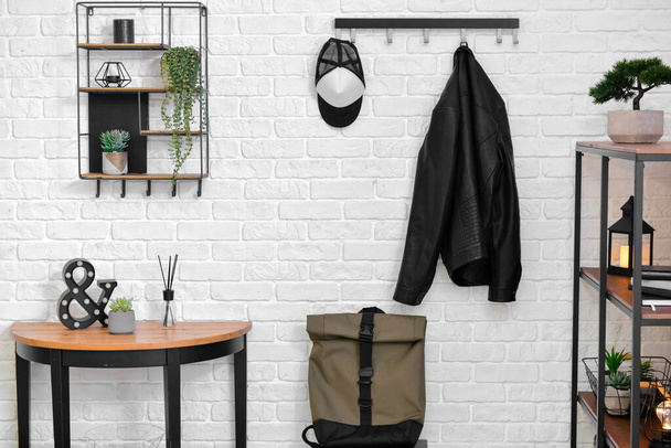Stylish interior of room with light brick wall, backpack and table with decor - 写真・画像