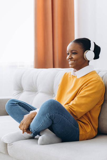 Odpocznij i zrelaksuj się. Spokojny czarny kobieta siedzi na worek fasoli, słuchając muzyki, audiobooka, podcast, korzystających medytacji snu i spokojny umysł w słuchawkach bezprzewodowych, pochylając się do tyłu, przestrzeń kopiowania - Zdjęcie, obraz