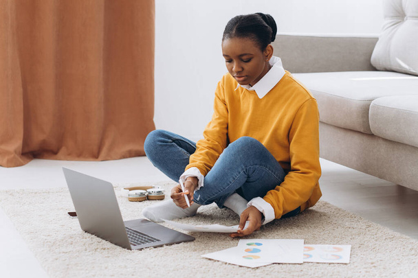 Linda jovem estudante universitária negra sentada no chão, bebendo café e fazendo projeto no laptop - Foto, Imagem