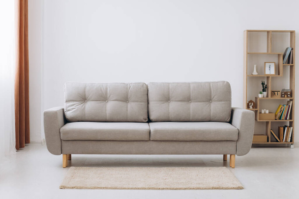Interior de la sala de estar minimalista blanco con sofá en un suelo de madera, decoración en una gran pared, paisaje blanco en la ventana. Inicio interior nórdico. - Foto, Imagen