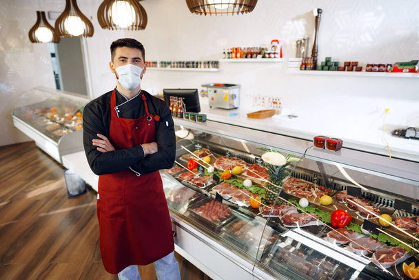 Portrait of a young man shopkeeper standing by meat stall in supermarket - Фото, зображення
