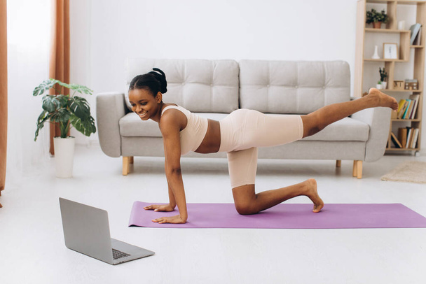 Exercício doméstico. Jovem mulher negra desportiva fazendo exercício de prancha em casa, treinando na sala de estar - Foto, Imagem