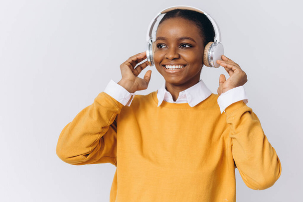 Gioioso positivo giovane donna afroamericana indossa cuffie stereo wireless ascolta la traccia audio. Persone emozioni felici e concetto di svago - Foto, immagini