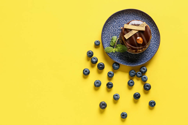 Bord met heerlijke chocoladetaart en bosbessen op gele achtergrond - Foto, afbeelding
