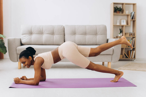 Domácí cvičení. Mladá sportovní černošky žena dělá prkno cvičení doma, školení v obývacím pokoji - Fotografie, Obrázek