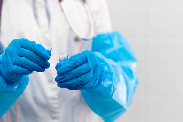 Az orvos keze gumikesztyűben egy ampulla gyógyszert tart a kórházban a koronavírus járvány idején. Szelektív fókusz. Közelkép - Fotó, kép