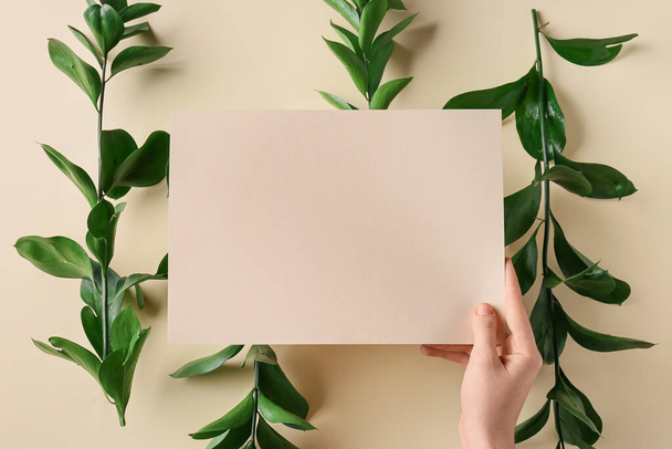 Female hand with blank card and plant branches on color background, closeup - Photo, Image