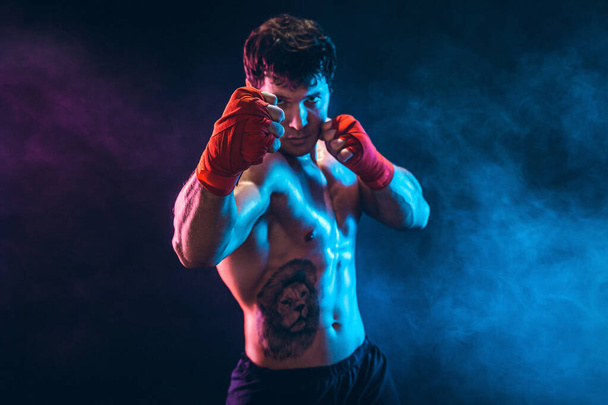 Portrait of muscular kickbox or muay thai fighter who punching on smoke background. Sport concept. - Foto, Imagem