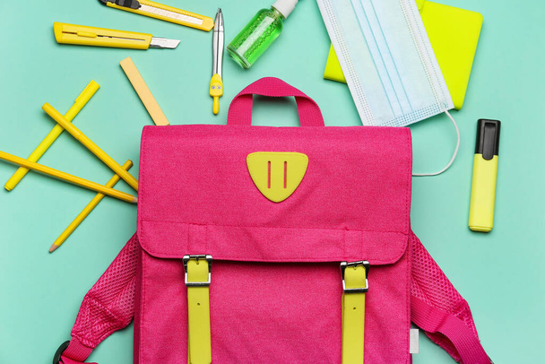 Школьный рюкзак, канцелярские принадлежности, медицинская маска и дезинфицирующее средство на цветном фоне, крупный план - Фото, изображение
