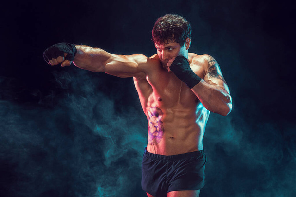 Half length of muscular boxer who training and practicing jab on smoke background. Sport concept - Valokuva, kuva