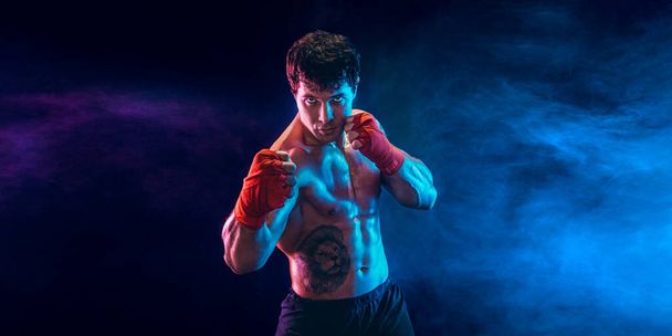 Half length muscular kickbox or muay thai fighter who punching on smoke background. Sport concept. - Foto, afbeelding