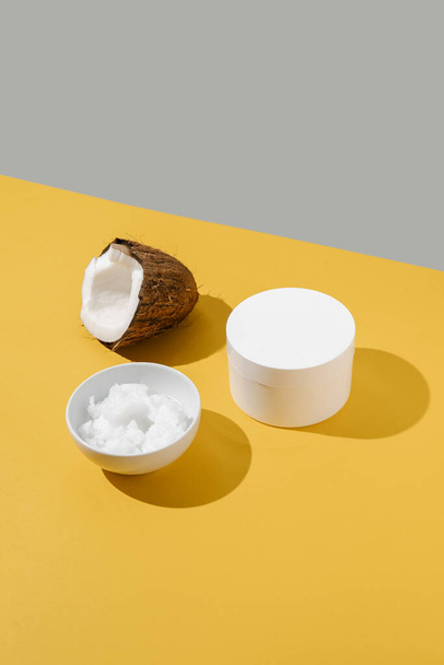 Half a coconut, coconut oil and a jar of coconut cream on a yellow background. - Φωτογραφία, εικόνα