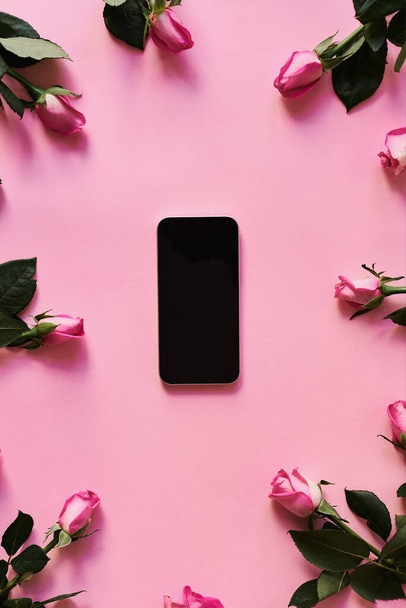 Κινητό τηλέφωνο και τριαντάφυλλο λουλούδια σε ροζ φόντο. Online προώθηση επίπεδη θέσει. Εαρινή περίοδος - Φωτογραφία, εικόνα