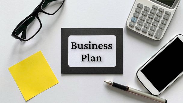 Business plan text on notepad with glasses, calculator, phone and yellow sticky note background. Business concept. - Photo, Image
