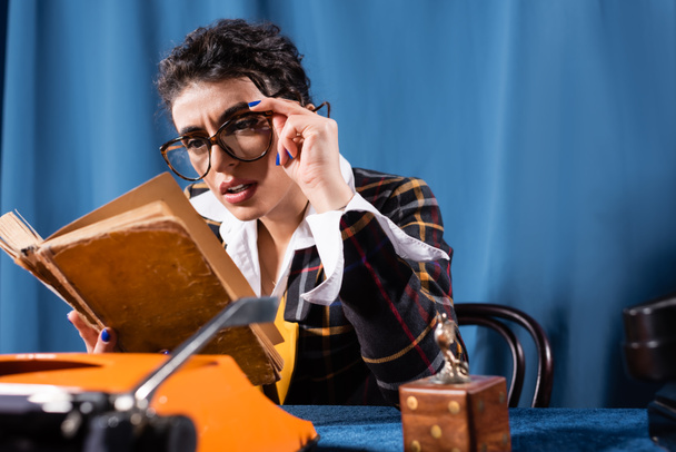 vintage style newswoman in eyeglasses reading book on blue background - Foto, Imagem