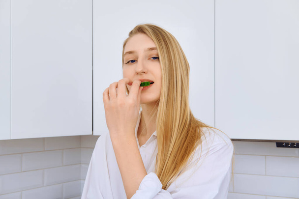 Tricky woman bite piece of cucumber while making vegetable salad - Foto, Imagem