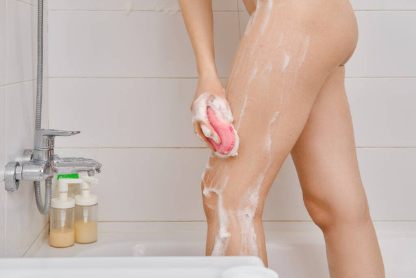 Banyoda bacaklarını süngerle yıkayan tanınmayan bir kadın. - Fotoğraf, Görsel