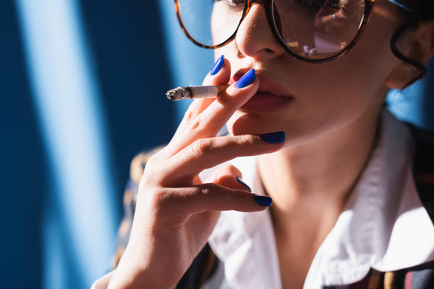cropped view of vintage style woman with blue manicure smoking on blurred background - Fotó, kép