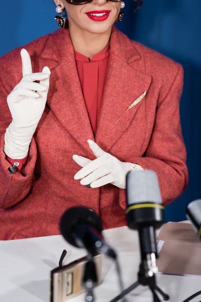 partial view of vintage style woman pointing with fingers near microphones during interview of blue background - Photo, Image