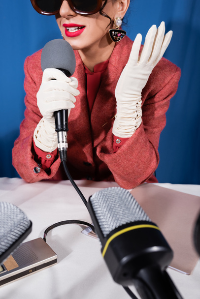 Mavi arka planda röportaj yaparken mikrofonla konuşan retro tarzı kadının kırpılmış görüntüsü - Fotoğraf, Görsel