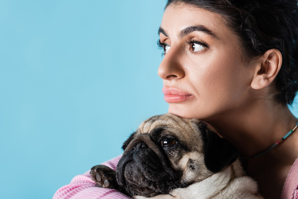 close up view of pensive woman looking away near pug dog isolated on blue - Photo, Image