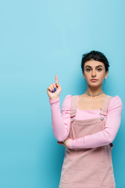 young and stylish woman pointing up with finger on blue background - Foto, Bild