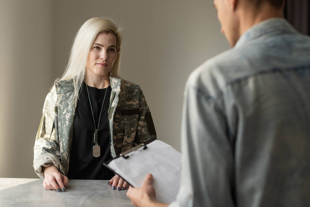 Mulher militar patriótica. Jovem militar patriótica falando com psicólogo fazendo anotações
 - Foto, Imagem