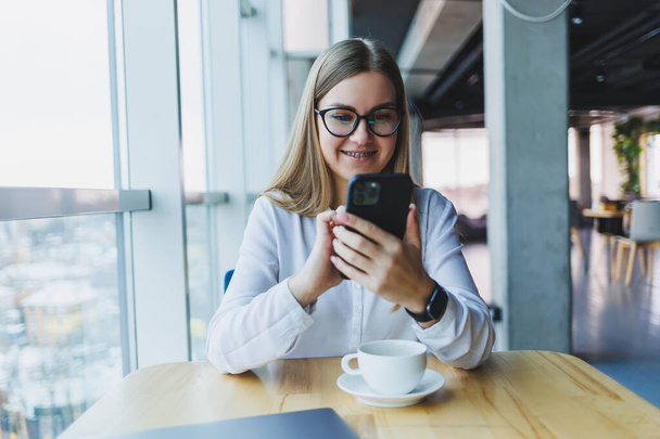 Χαρούμενη χαμογελαστή γυναίκα διευθυντής χρησιμοποιώντας το κινητό τηλέφωνο gadget για να ελέγξετε την υπηρεσία παράδοσης μέσω online app, δωρεάν 4g ασύρματο δίκτυο στην καφετέρια, χαρούμενα μηνύματα freelancer στο κινητό τηλέφωνο - Φωτογραφία, εικόνα