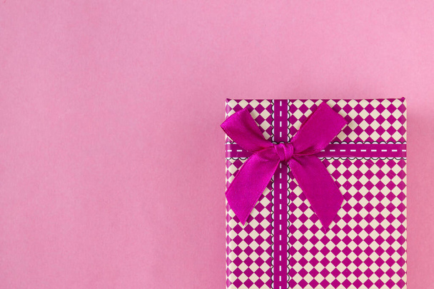 Geschenkbox mit scharlachrotem Band auf rosa Hintergrund, Nahaufnahme - Foto, Bild