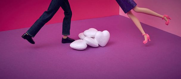 The dolls, a woman and a man, fall towards each other over a pile of hearts. Purple, violet, red, pink background. Text space. Passion, fall in love, valentine's day, concept. Minimal style. - Foto, imagen