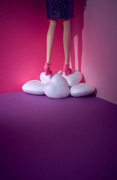 A woman, a doll, climbs over a pile of hearts on a violet pink background. Text space. Feelings, love, Valentine's Day, concept. Minimal style. - Photo, Image