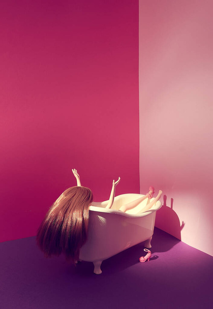 Жіноча лялька у ванній. Червоне волосся. Підняті руки і ноги. Рожеве взуття. Яскраво-фіолетовий рожевий фон. Простір тексту. Релаксація, самовідданість, концепція. Мінімальний стиль
. - Фото, зображення