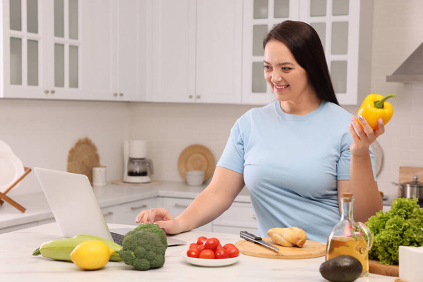 Beautiful overweight woman following online recipe to prepare healthy meal in kitchen - Foto, Imagem