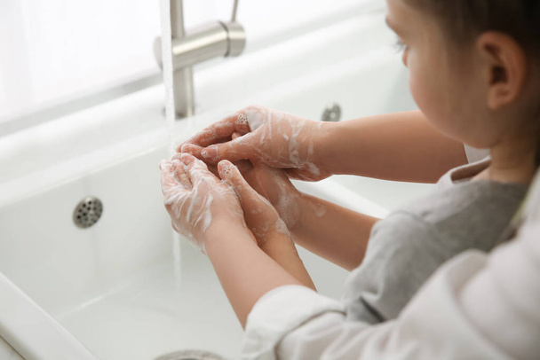 Mother and daughter washing hands with liquid soap together at home, closeup - Fotó, kép