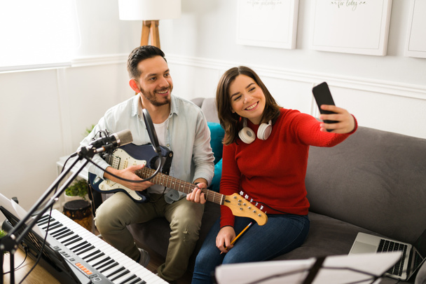 Musikerfreunde machen neue Musik. Glückliche kaukasische Frau macht ein Selfie mit einem attraktiven Mann, der Gitarre spielt  - Foto, Bild