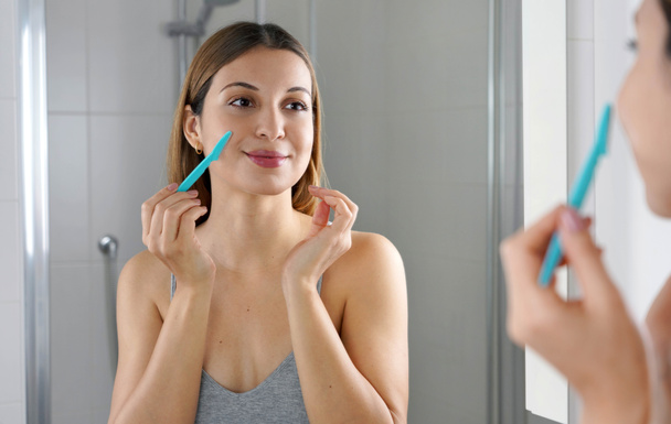 A szépséges nő borotvával borotválja az arcát otthon. A csinos lány borotvát használ a fürdőszobában. Arcszőrtelenítés. - Fotó, kép