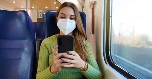 Χαλαρωμένος επιβάτης τρένου χρησιμοποιώντας εφαρμογή smartphone κατά τη διάρκεια μετακίνησης φορώντας προστατευτική μάσκα προσώπου. Πανοραμική πανό των ανθρώπων που μετακινούνται μετά την εργασία. - Φωτογραφία, εικόνα