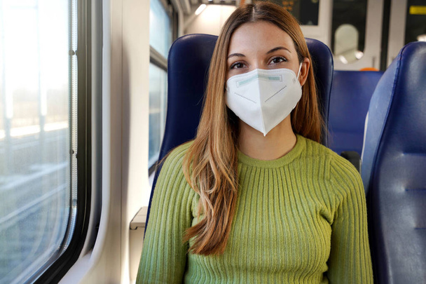 Movilidad urbana y seguridad en un mundo COVID-19. Mujer joven y feliz con máscara médica sentado en el tren mirando a la cámara. - Foto, imagen