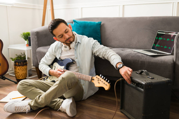 Όμορφος νεαρός άνδρας που χρησιμοποιεί ενισχυτή ενώ παίζει ηλεκτρική κιθάρα στο σπίτι  - Φωτογραφία, εικόνα