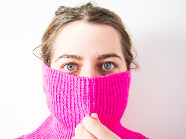 the face of a beautiful girl covered by the throat of a pink sweater - Zdjęcie, obraz