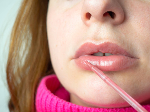 Κοντινό πλάνο ενός κοριτσιού που χρησιμοποιεί υγρό κραγιόν ή lip balm, καλλυντικά για την περιποίηση των χειλιών. - Φωτογραφία, εικόνα