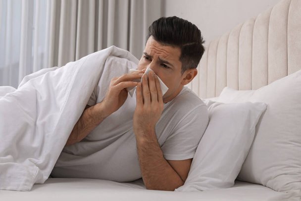 Sick man with tissue suffering from cold in bed at home - Fotó, kép