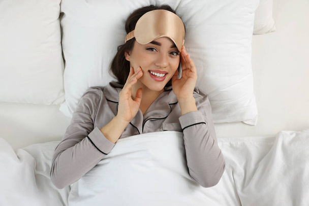 Beautiful young woman with sleeping mask lying in bed, top view - Φωτογραφία, εικόνα