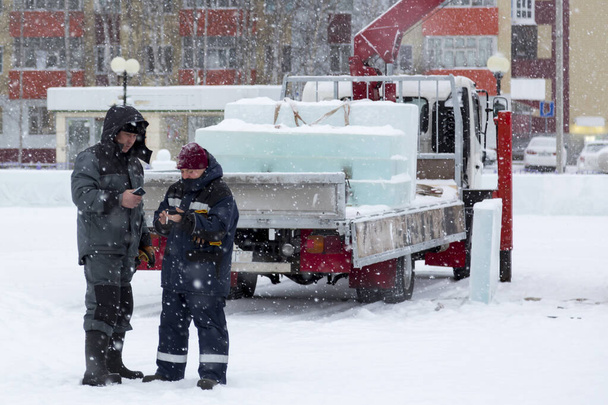 Os funcionários em um guindaste de caminhão olham para telefones celulares em uma queda de neve em um local de construção - Foto, Imagem