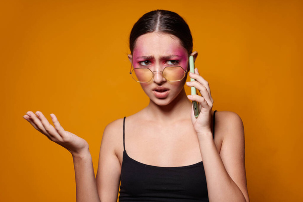 pretty woman with phone pink face makeup posing attractive look glasses yellow background unaltered - Photo, image