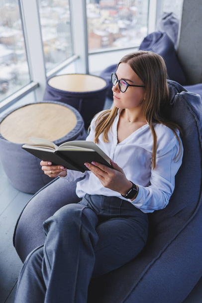 Break. Smiling young woman in glasses relaxing on bean bag chair sitting at table and relaxing using notepad, happy woman leaning back enjoying work feeling satisfied - Foto, imagen